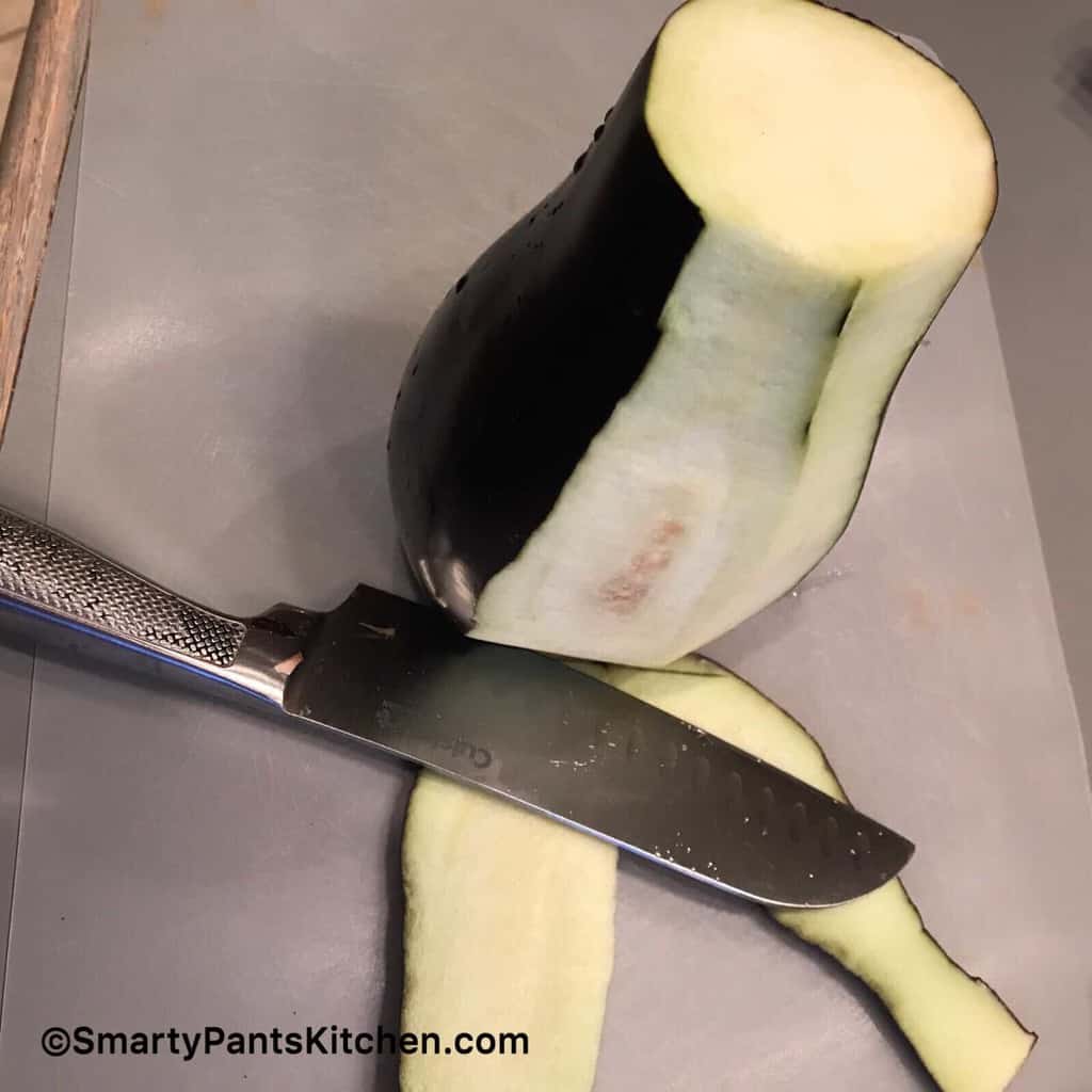 Eggplant on cutting board with knife removing skin