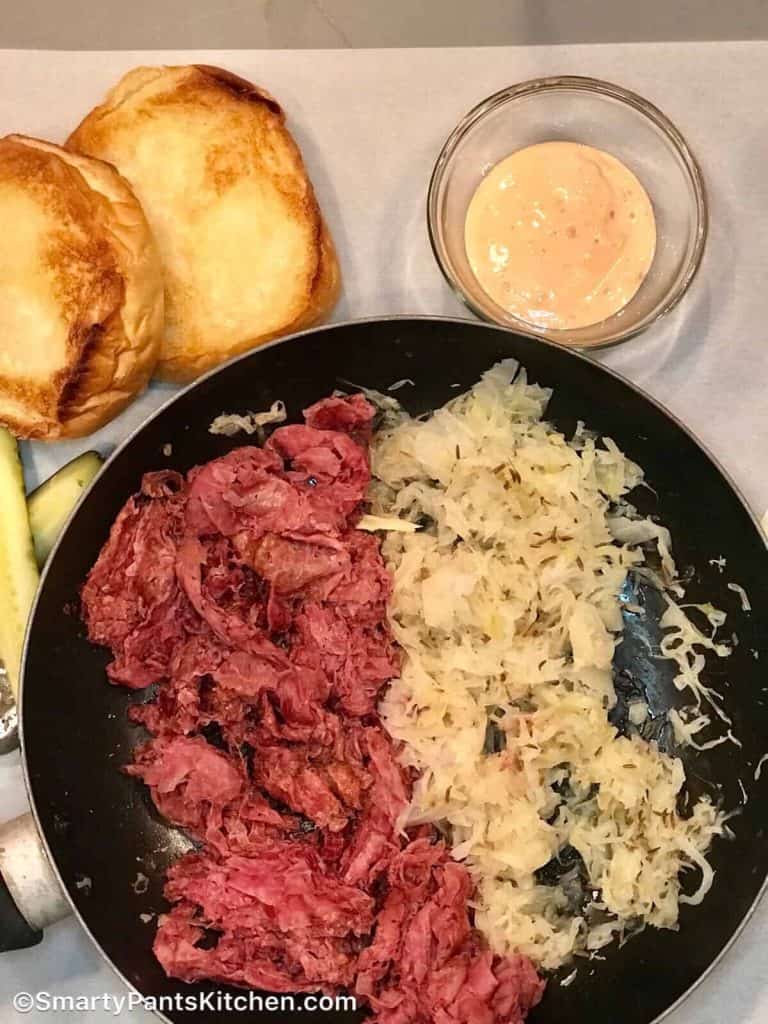 Pastrami and sauerkraut in a skilllet with a side of toasted buns and
