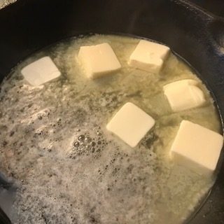 A cup of flour, a stick of butter, a whisk and a wooden spoon in a cast iron skillet..