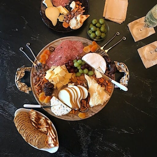 Round wooden serving tray with cheese, grapes, salami and serving utensils