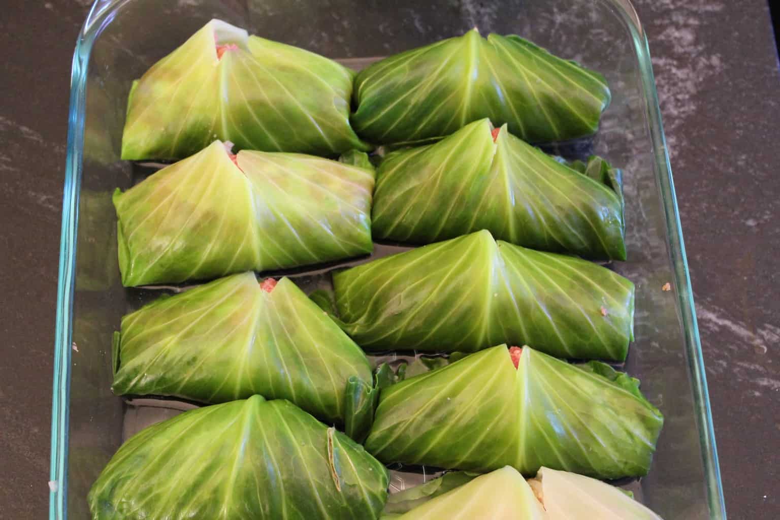 12 stuffed grape leaves in a baking dish.