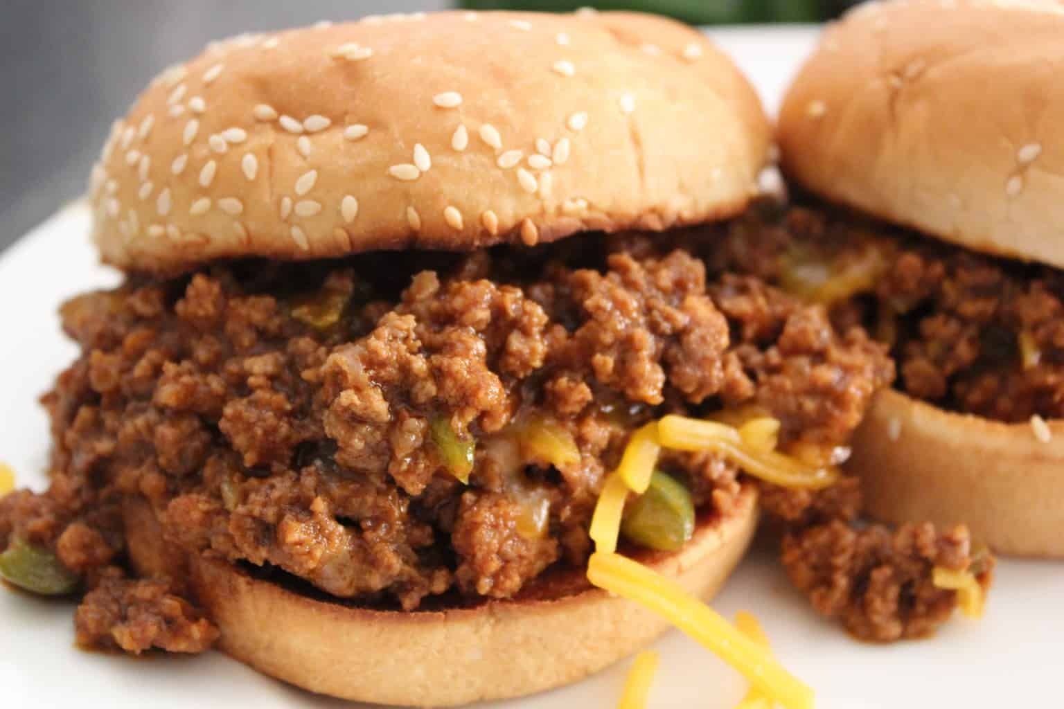 Sloppy Joe with shredded cheese and a sesame bun on white plate