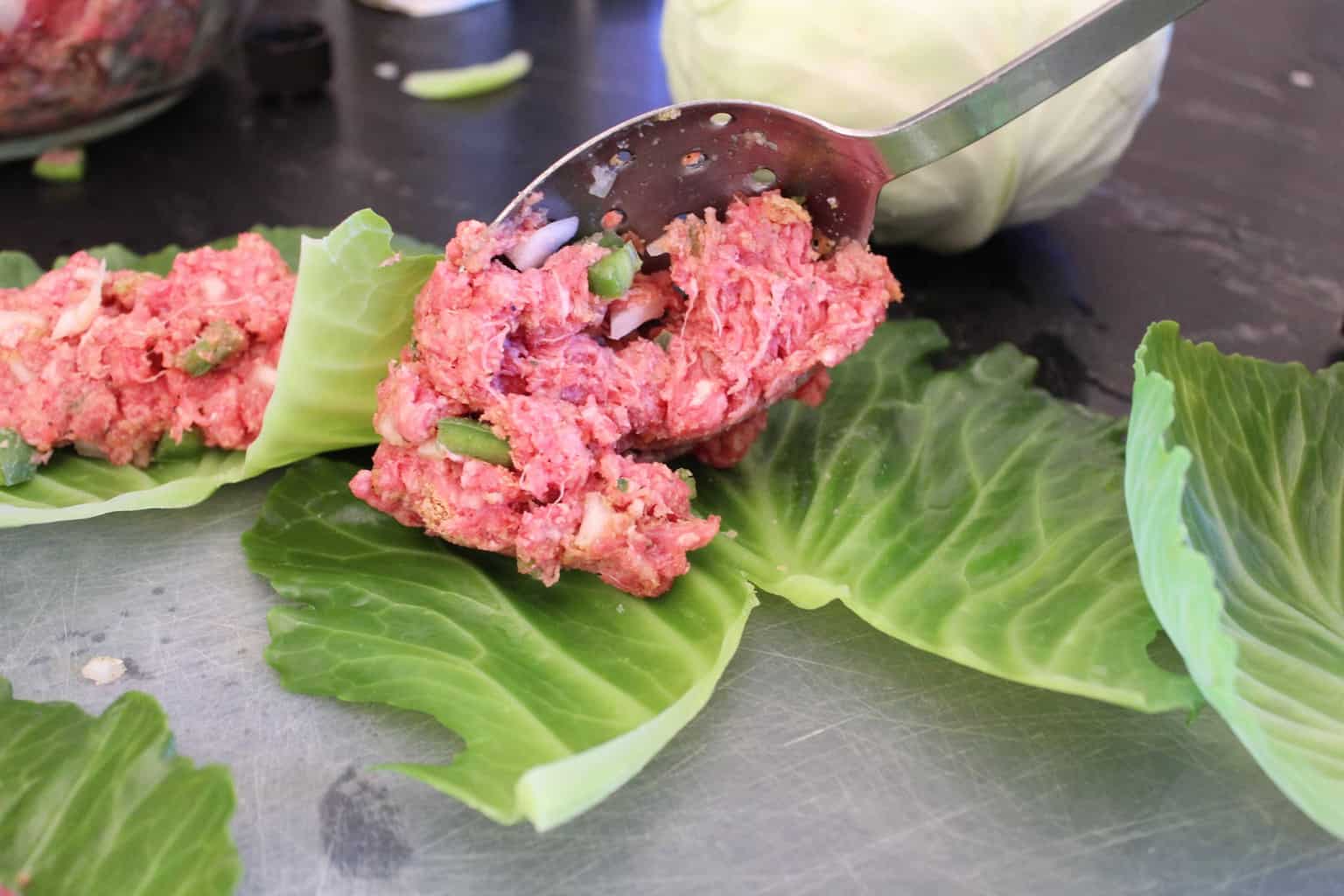 Meat mixture being spooned onto leaf.