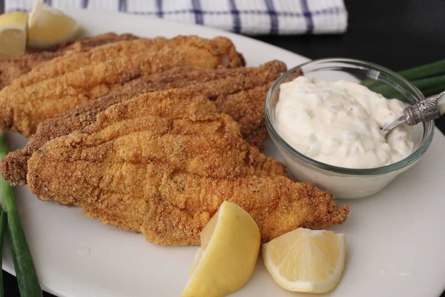 Fried catfish with a side of tartar sauce and lemon on white plate