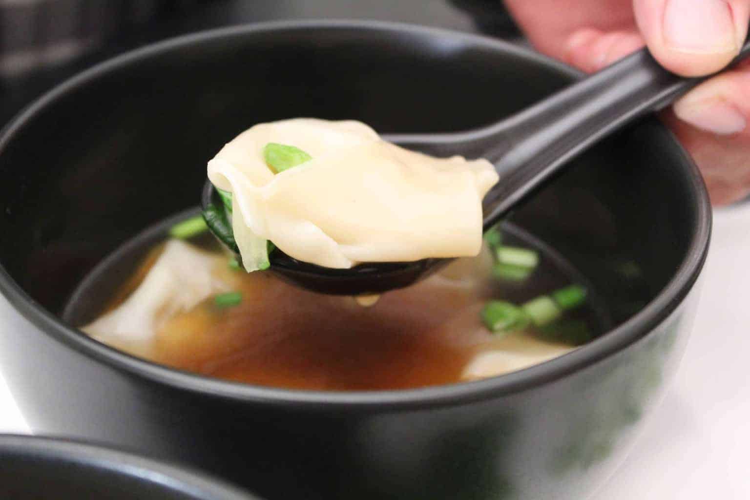 won ton soup in a black bowl.