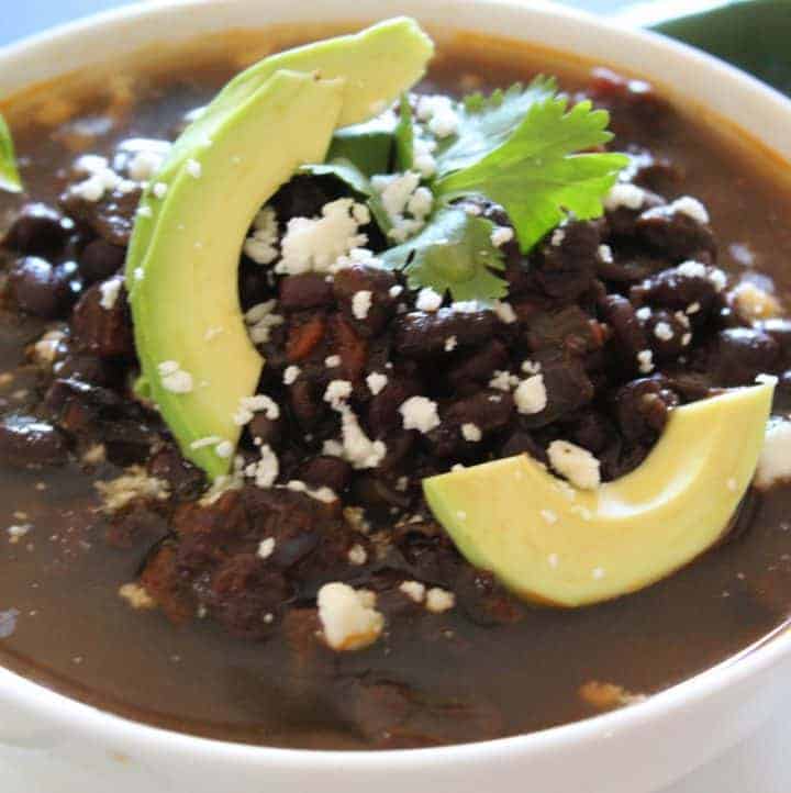 Black beans in a white bowl garnished with sliced avocado.