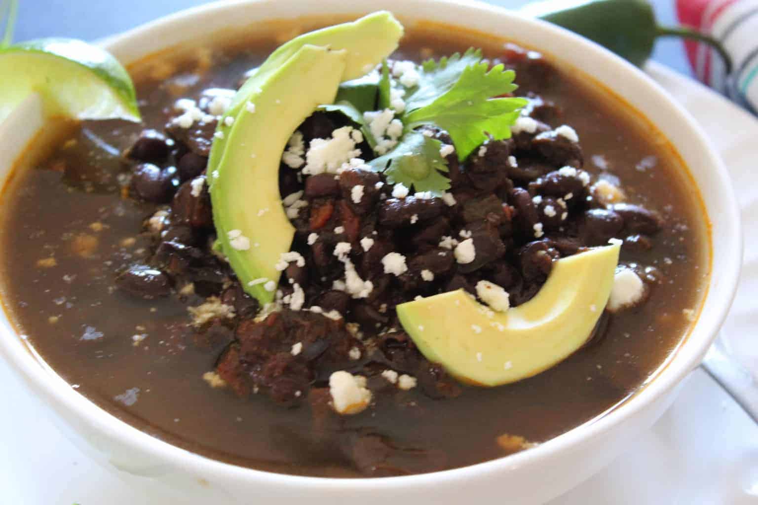 Black beans in a white bowl garnished with sliced avocado.