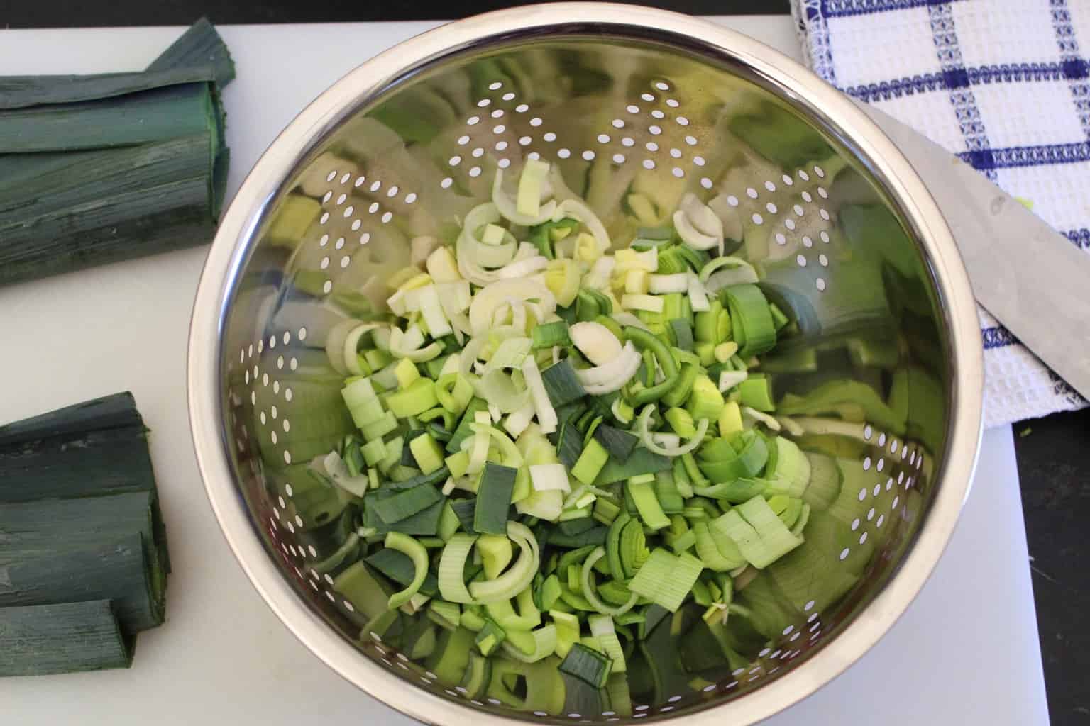 Sliced leeks in colander being rinsed with water