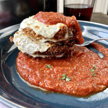 Crispy eggplant parmesan rounds stacked, topped with sauce and cheese.