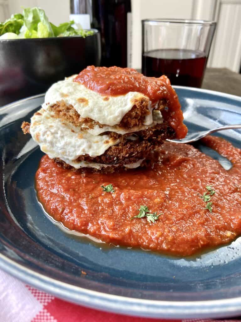 Crispy eggplant parmesan rounds stacked, topped with sauce and cheese.