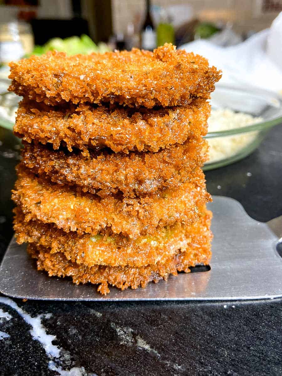 Crispy fried eggplant rounds stacked on stainless spatula