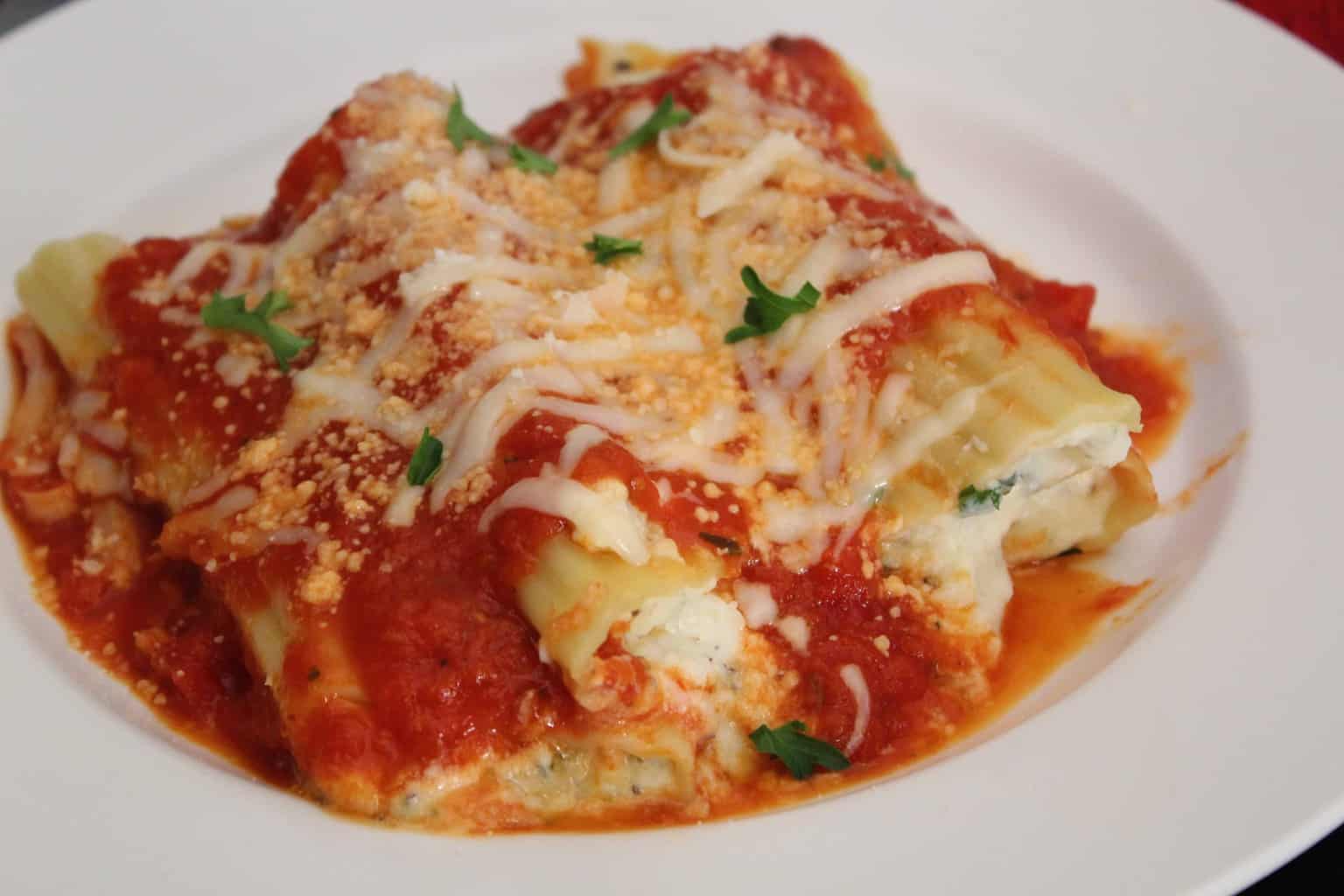 Manicotti topped with tomato sauce and cheese on white plate