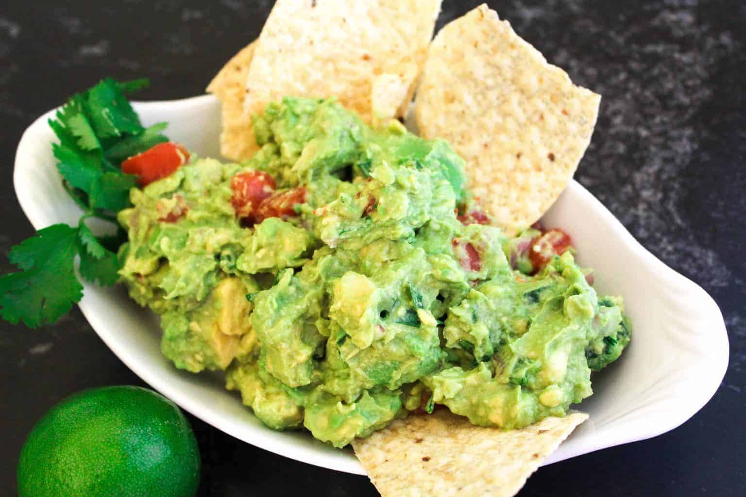 Guacamole in oval serving dish garnished with cilantro and chips.