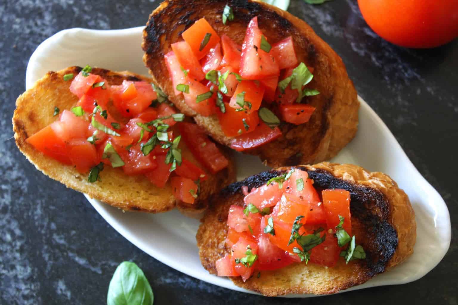 Three rounds of toasted Italian bread topped with bruschetta on a white oval plate