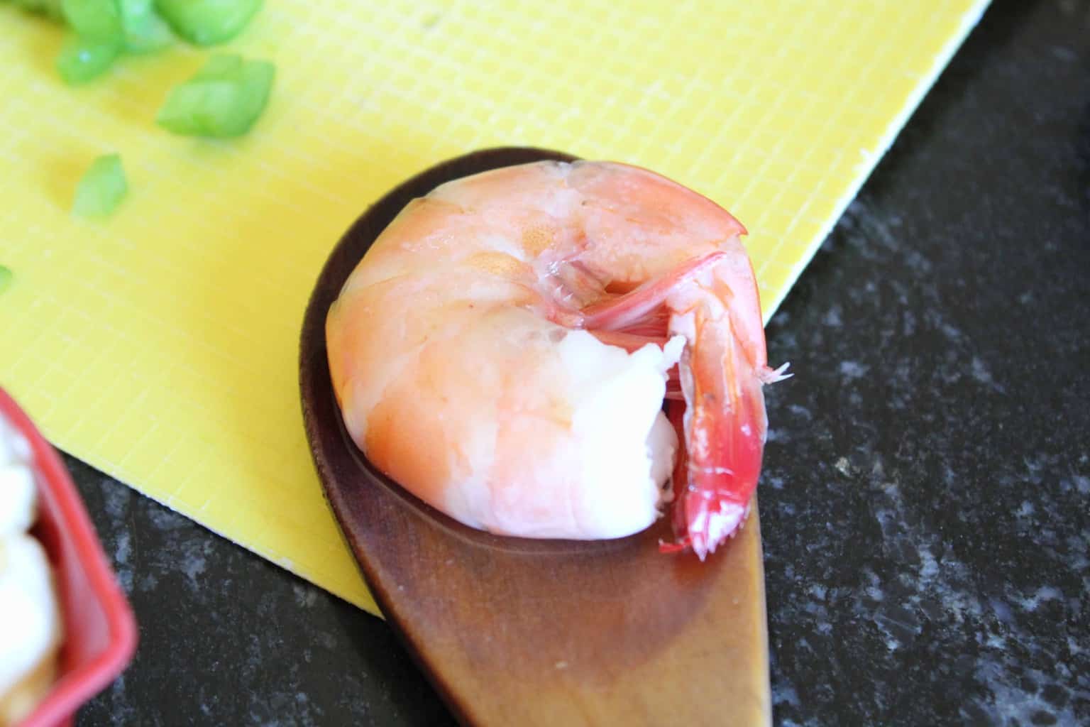 Cooked pink shrimp in shell on a wooden spoon