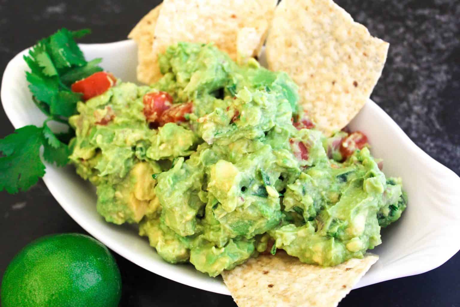Guacamole dip in a white serving bowl with tortilla chips.