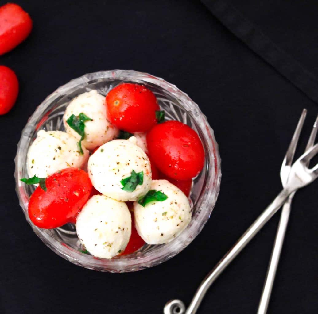 Grape tomatoes and mozzarella balls in a glass bowl with basil.