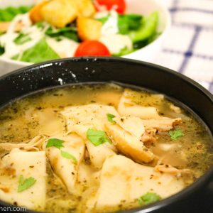 Chicken and dumplings in black bowl with side salad
