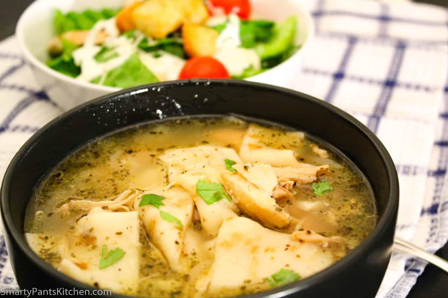 Chicken and dumplings in black bowl with side salad