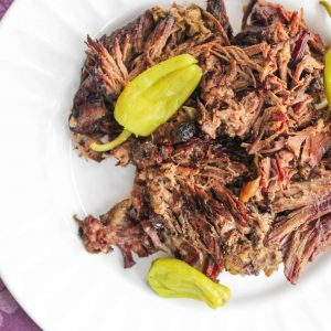 Shredded Mississippi Pot roast on a white plate with three pepperoncini peppers