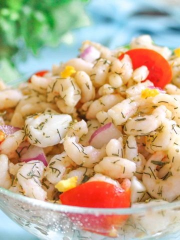 Seafood ceviche in glass bowl with dill weed and tomato garnish.