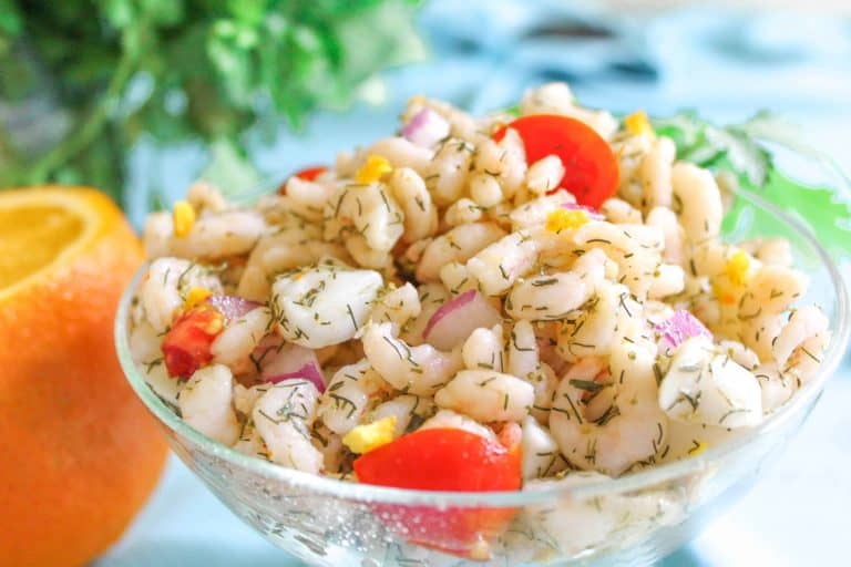 Seafood ceviche in glass bowl with dill weed and tomato garnish.
