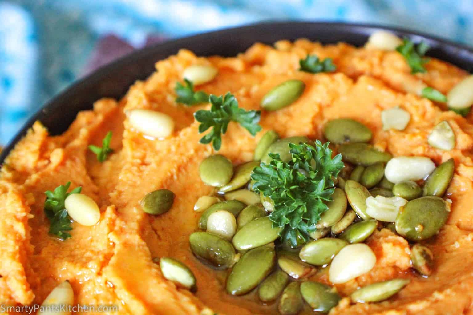 Pumpkin hummus in black bowl garnished with pumpkin seeds and pine nuts