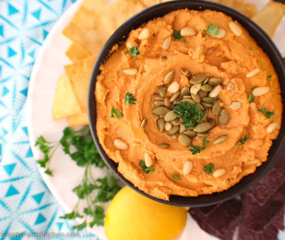 Pumpkin hummus in black bowl garnished with pepitas and pine nuts