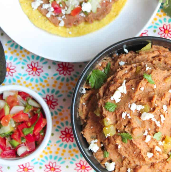 Refried beans in black bowl garnished with white cheese, cilantro and green chiles