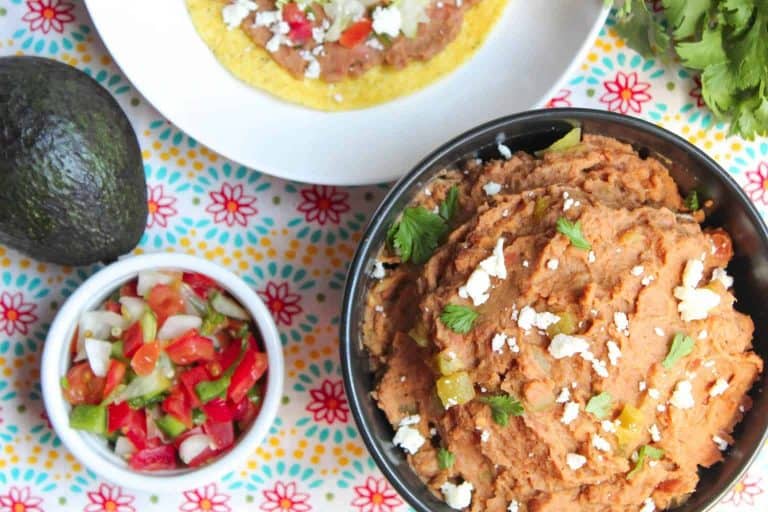 Refried beans in black bowl garnished with white cheese, cilantro and green chiles