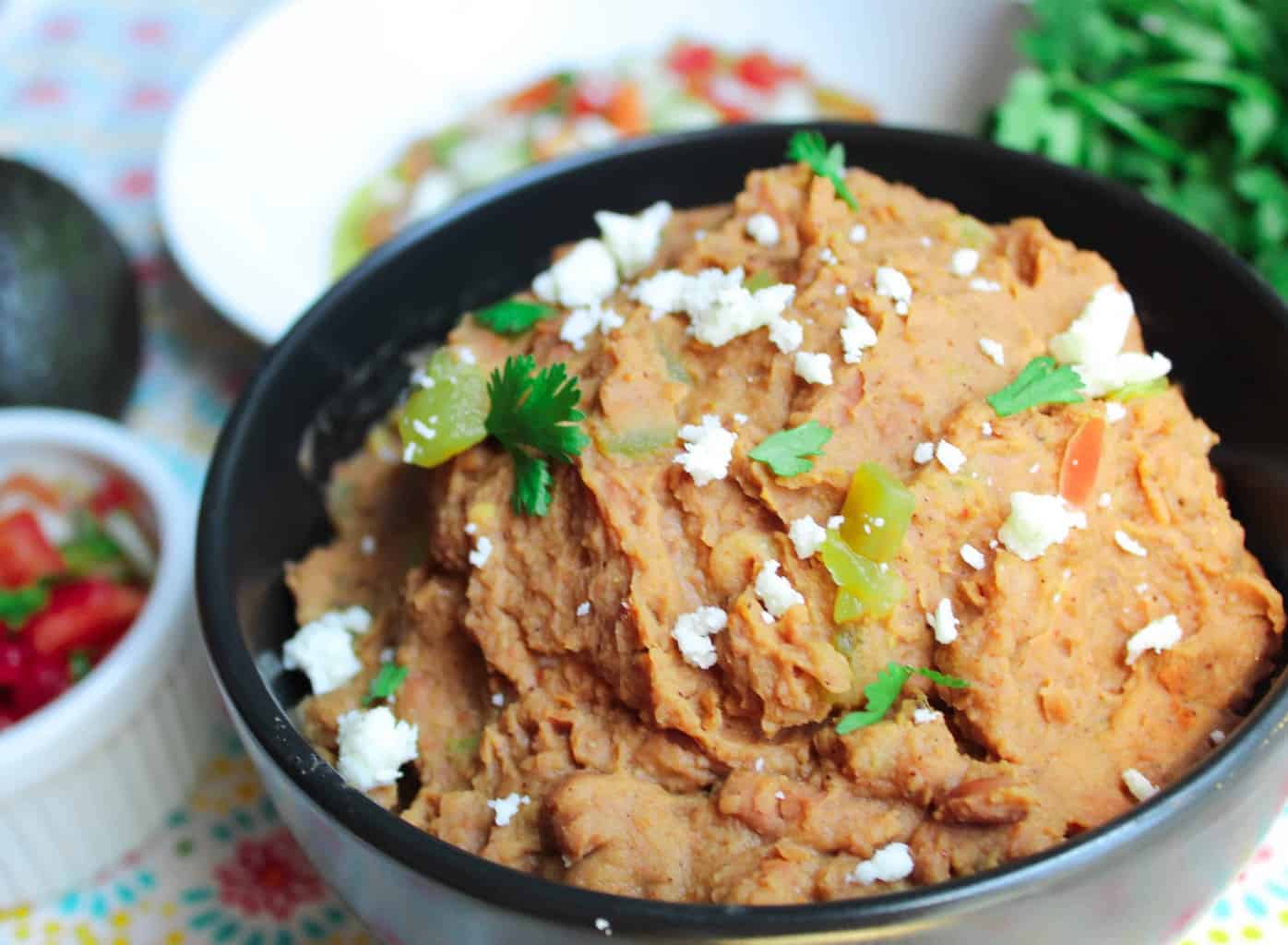 Refried beans in a black bowl garnished with white cheese, cilantro and green chiles.