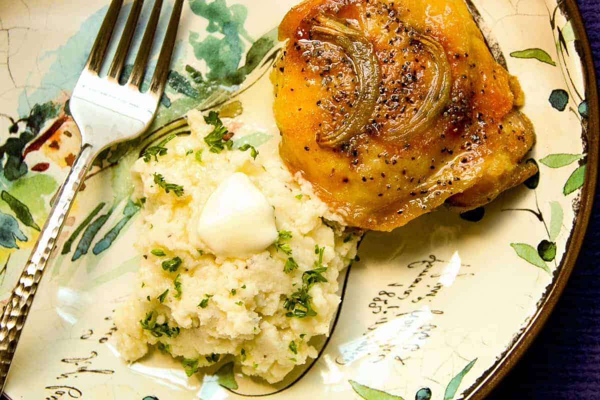 Oven baked chicken thighs with a side of mashed potatoes on colorful plate