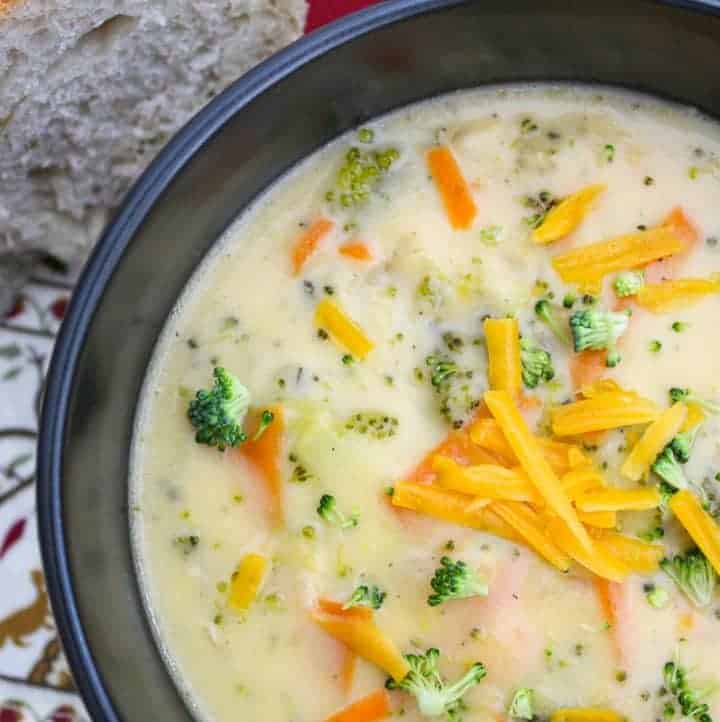 Organic Broccoli Cheese Soup in black bowl garnished with shredded cheese.