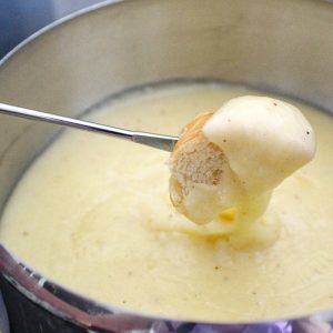 Skewer with bread dipped in fondue over cheese fondue