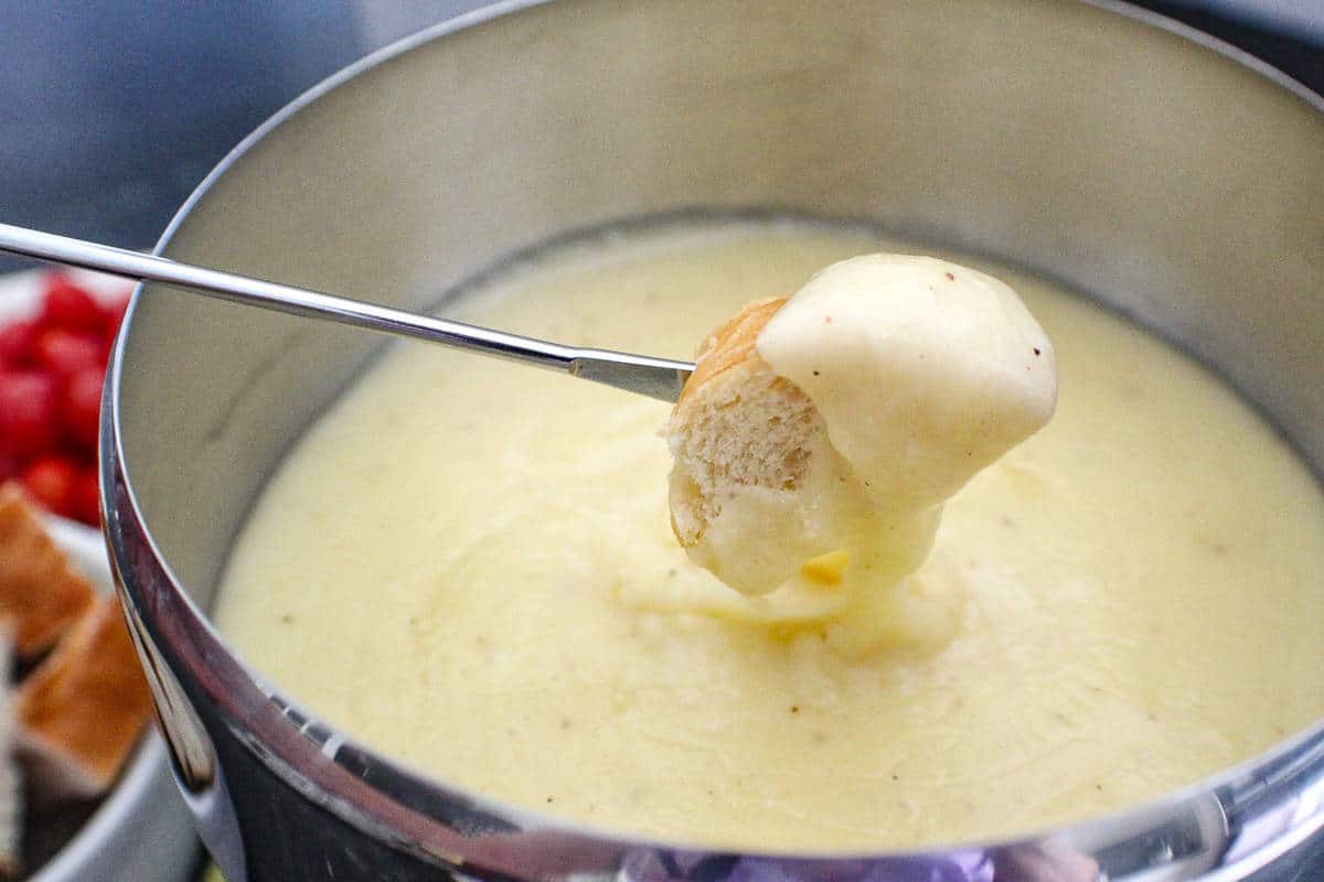 Bite of bread coated in fondue on skewer above fondue pot