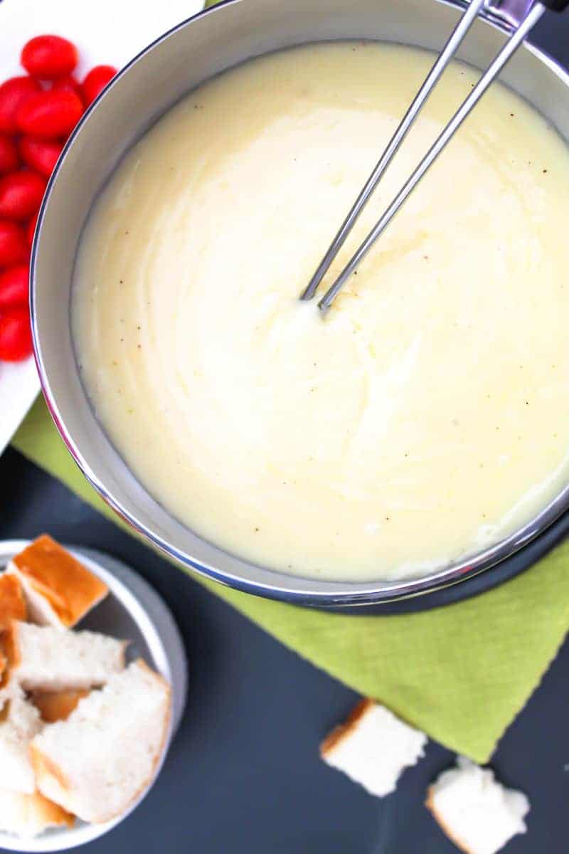 Cheese fondue in fondue pot with skewers, bread and tomatoes on the side