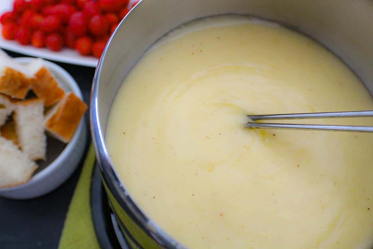 Two skewers in fondue with bread and cherry tomatoes on the side