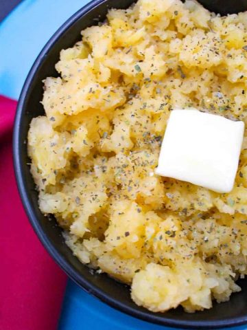 Mashed Ruttabagas in a black bowl with a melting pad of butter on top garnished with marjoram