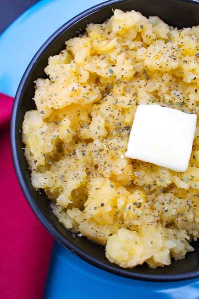 Mashed Ruttabagas in a black bowl with a melting pad of butter on top garnished with marjoram