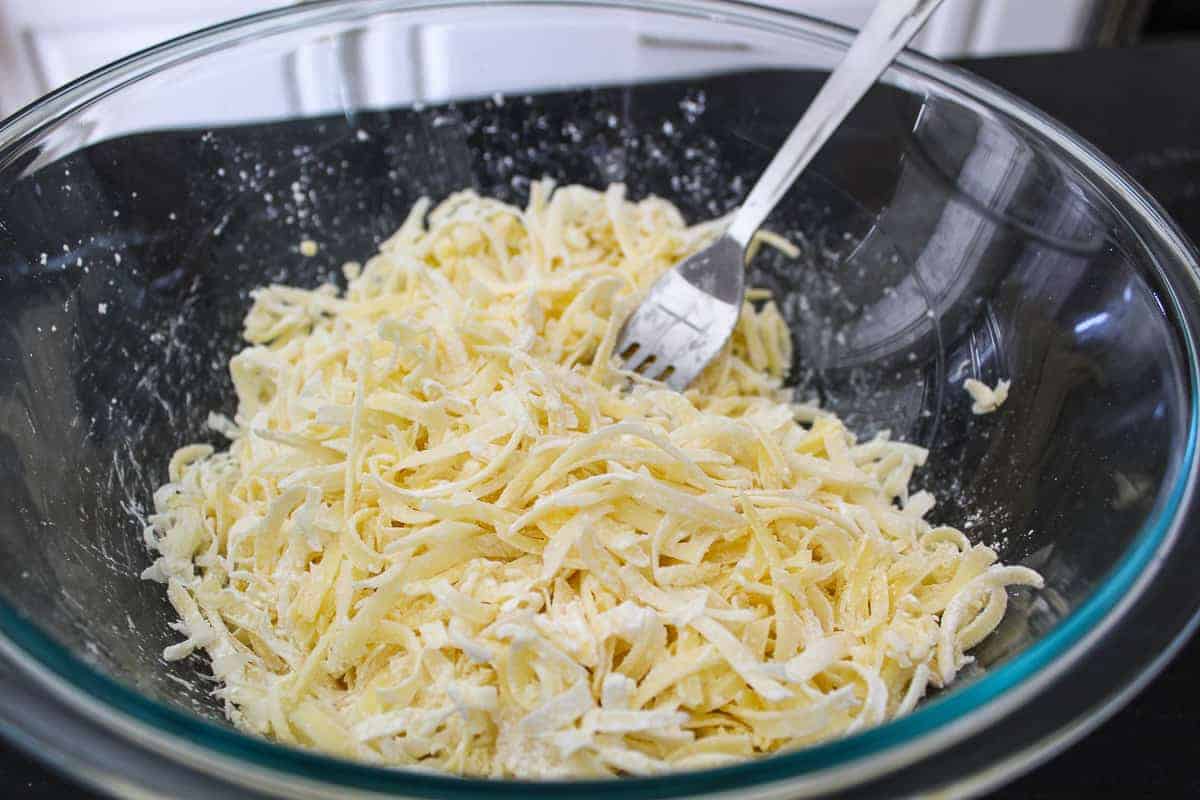 Shredded cheese coated with cornstarch in bowl and fork