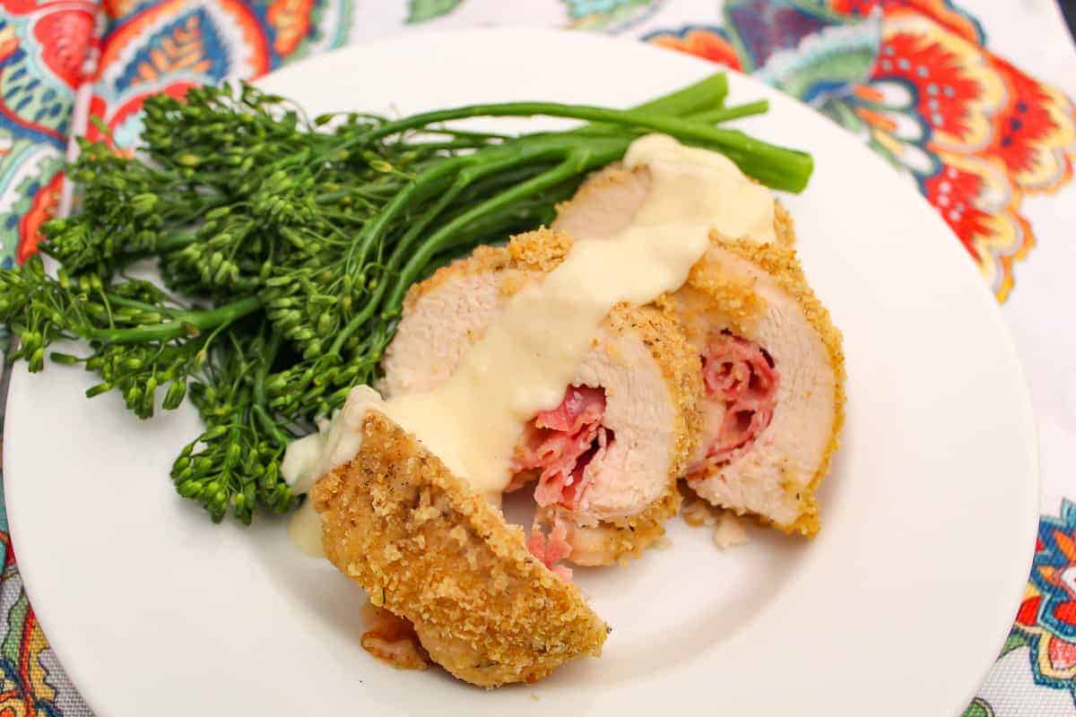 Sliced chicken cordon bleu with dijon sauce and a side of broccolini on a plate