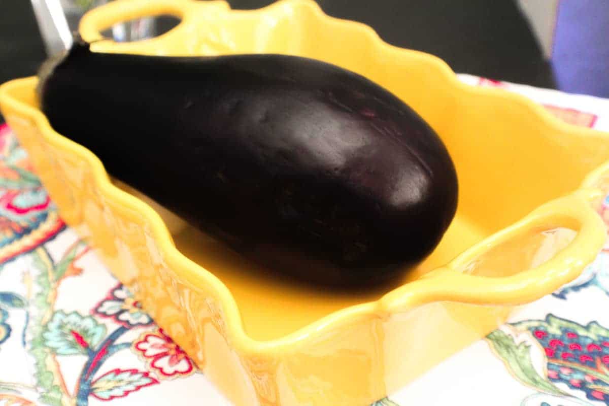 Whole eggplant in yellow baking dish.