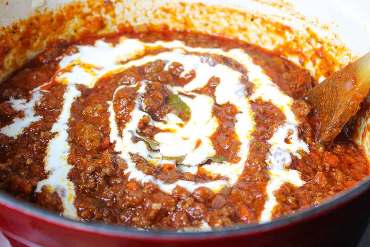 Cream drizzled over sauce in stockpot