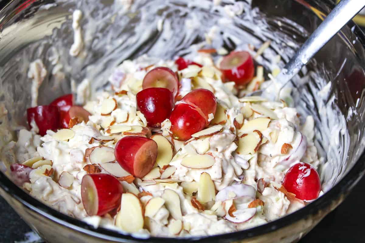 Turkey, chopped grapes, mayonnaise and almonds being mixed in a glass bowl with spatula