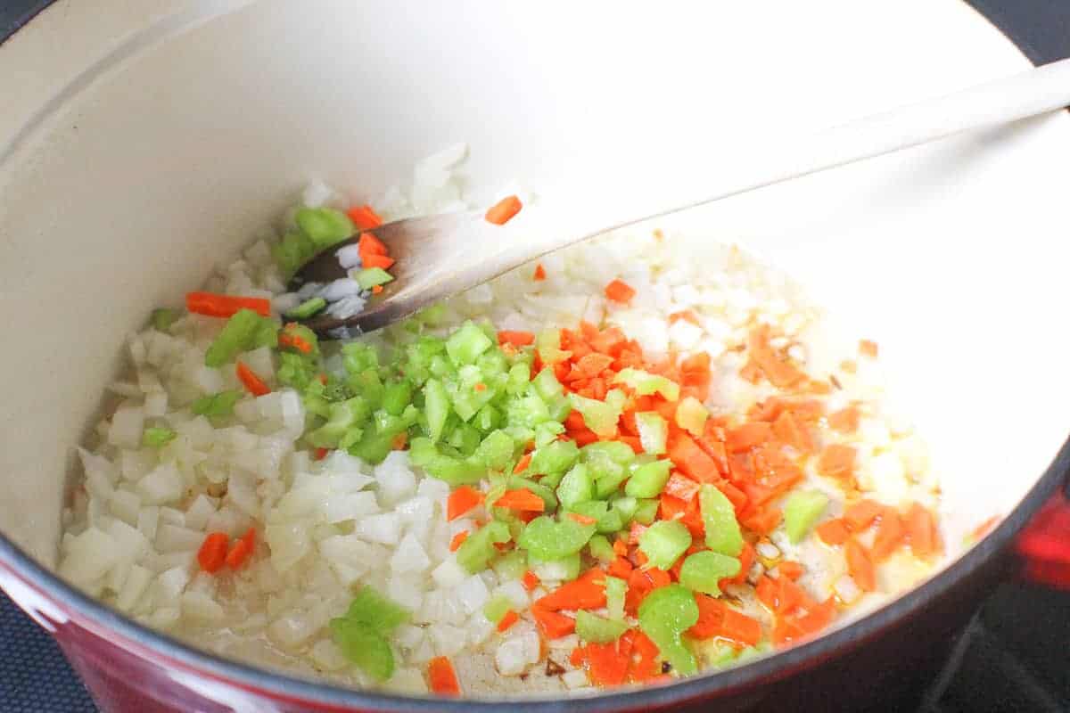 Chopped celery, carrots and onions in stockpot with wooden spoon