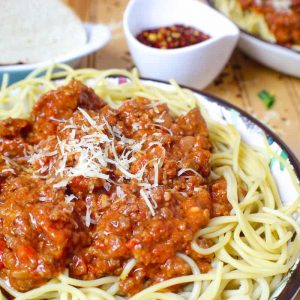 A bowl of pasta topped with bolognese sauce and parmesan cheese.