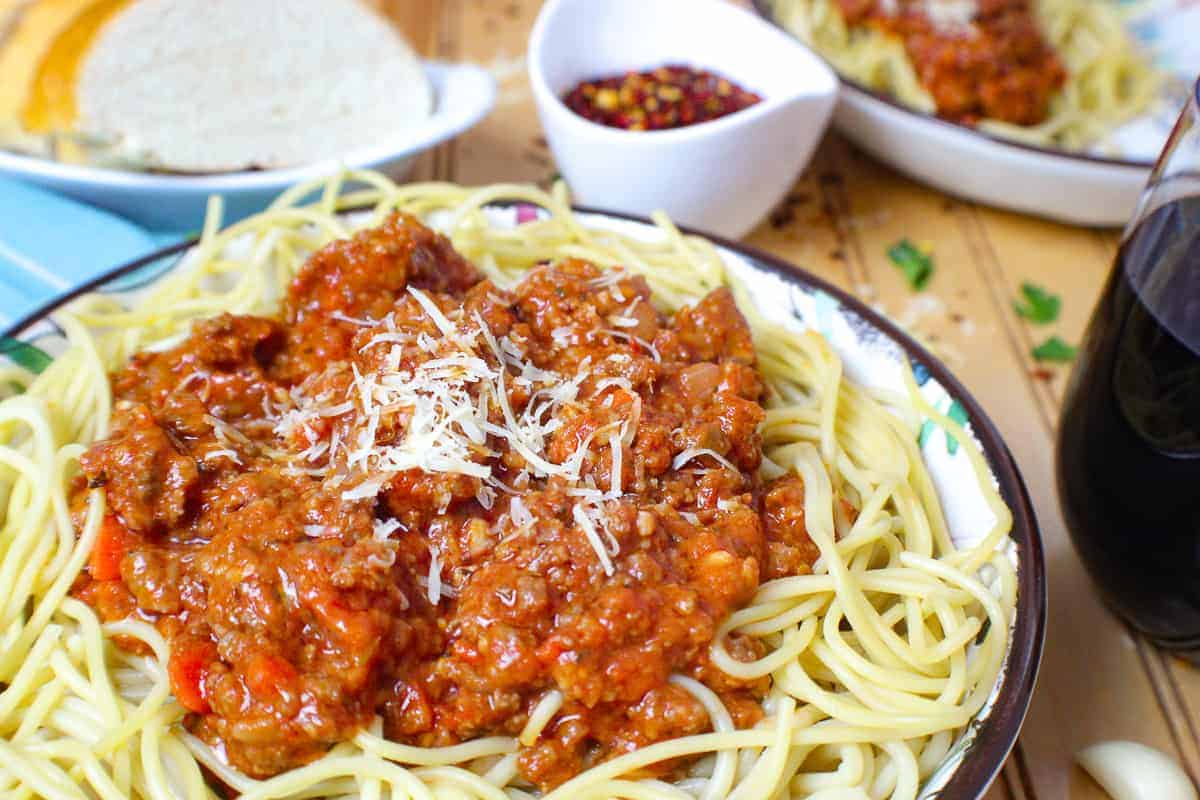 Round bowl of spaghetti noodles with bolognese sauce in the center, topped with parmesan cheese