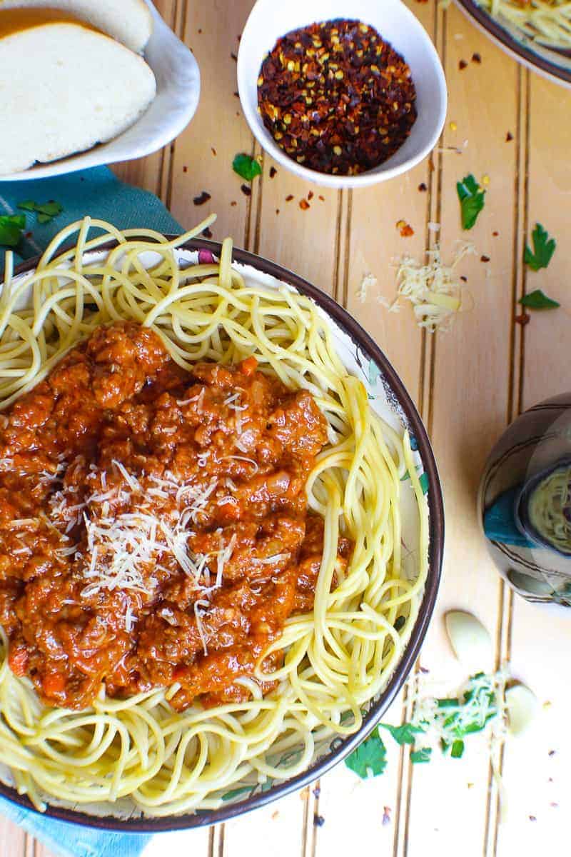 Bowl of spaghetti noodles topped with rich, thick meaty bolognese sauce and a side of bread