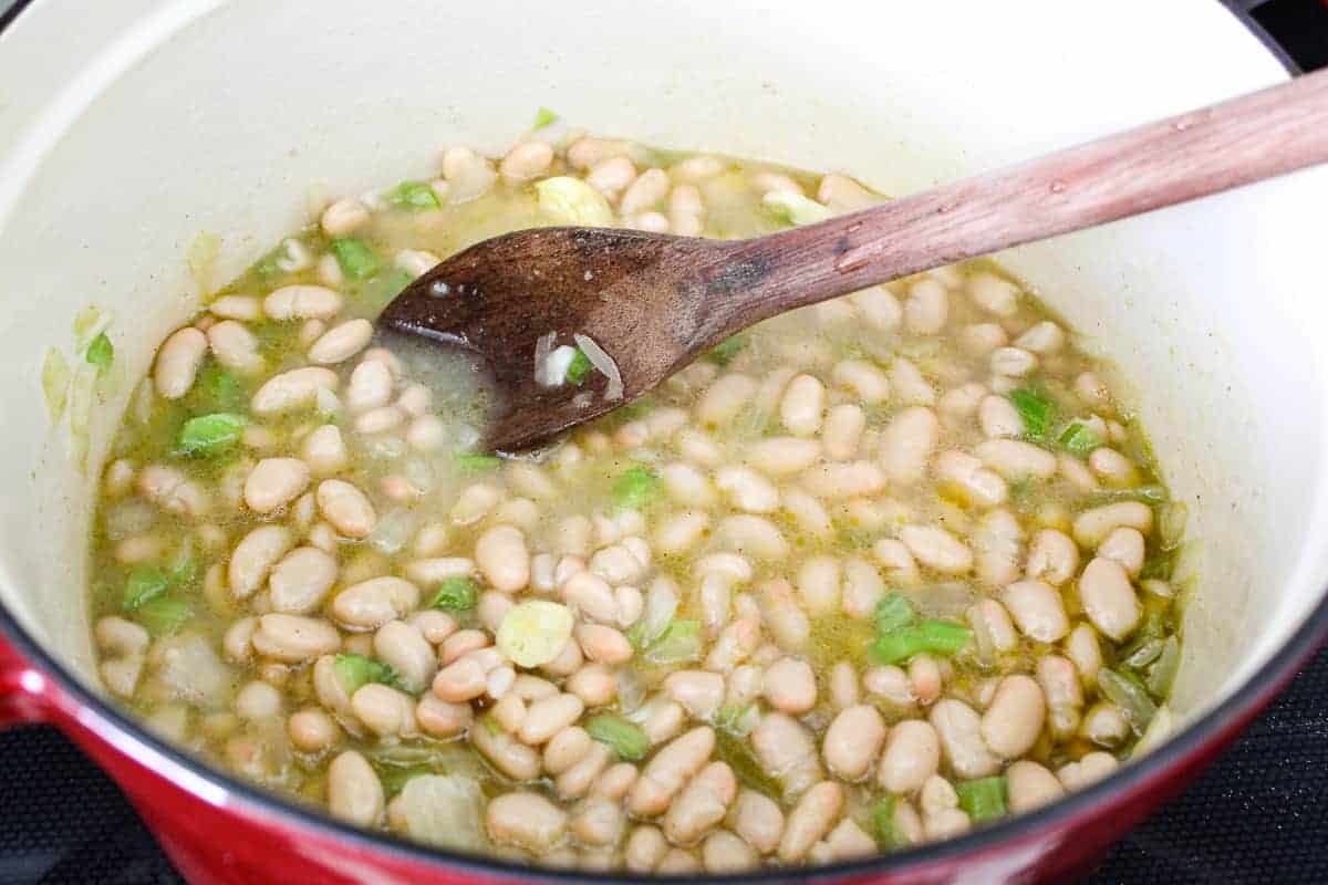 White beans, broth and vegetables in stockpot with wooden spoon.