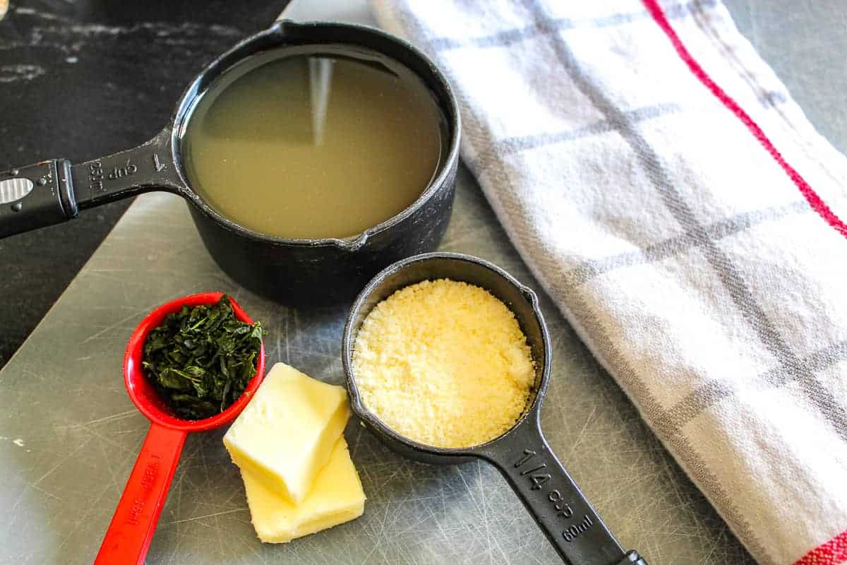 Butter, broth, parmesan cheese in measuring spoons on counter.